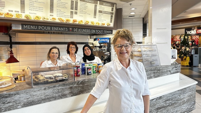 Une femme devant le comptoir d'un restaurant de la halte bouffe du Carrefour Rimouski. Trois de ses employées se trouvent derrière elle. 