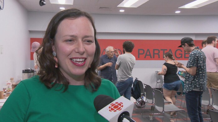 Jackie Smith parle au micro devant une salle remplie de chaises et de gens debout.