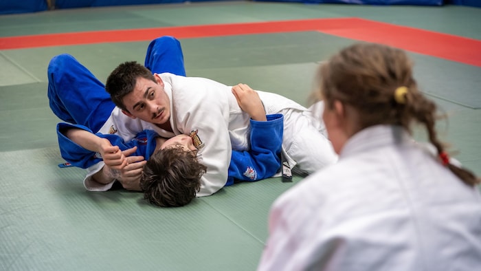 Un entraîneur de judo explique une manoeuvre au sol sur les tatamis d’un dojo.