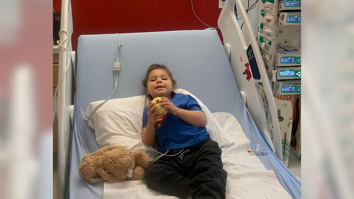 Le jeune garçon est dans un lit d'hôpital.