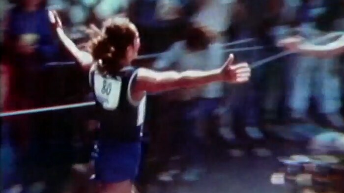 Jacqueline Gareau, de dos avec son dossard de course, les bras en l'air en courant.
