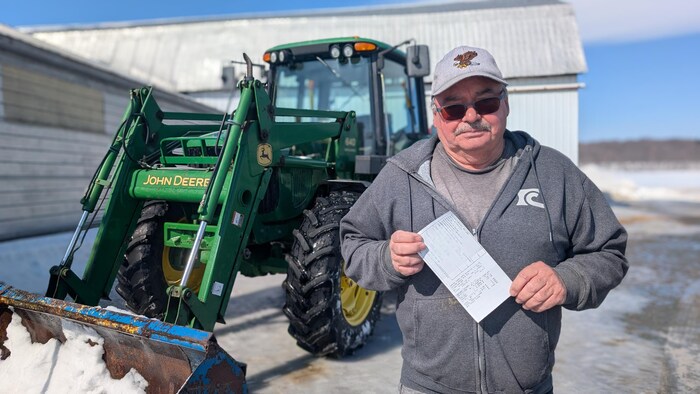 Un homme tient une facture devant un tracteur, dehors, en hiver.