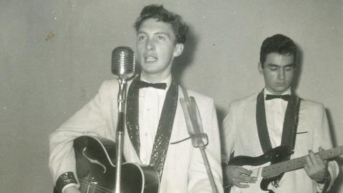 Jacques Michel chante au micro en jouant de la guitare.