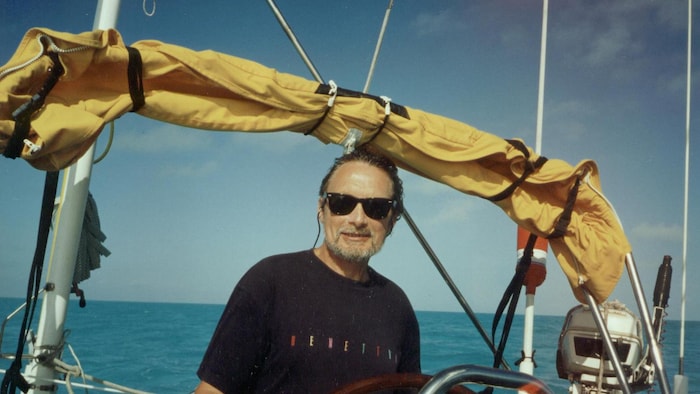 Jacques Michel pose derrière la barre de son voilier.