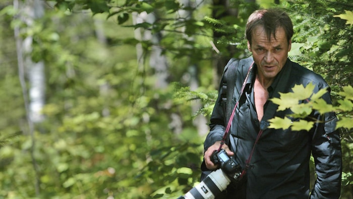 Jacques Nadeau avec son appareil photo dans un boisé.