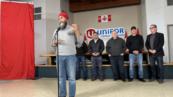 Jagmeet Singh, standing, speaks in front of a microphone