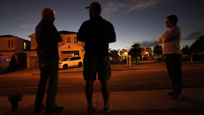 Trois hommes attendent devant une maison alors que le soleil se couche.