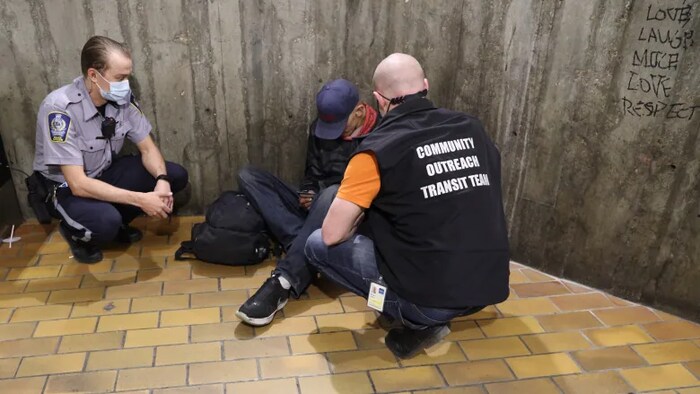 Un agent de la paix et un travailleur social discutent avec une personne dans une station de train léger d'Edmonton (juin 2022).
