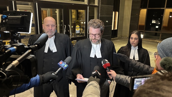 Un avocat lit une déclaration aux journalistes, entouré de deux de ses collègues. 