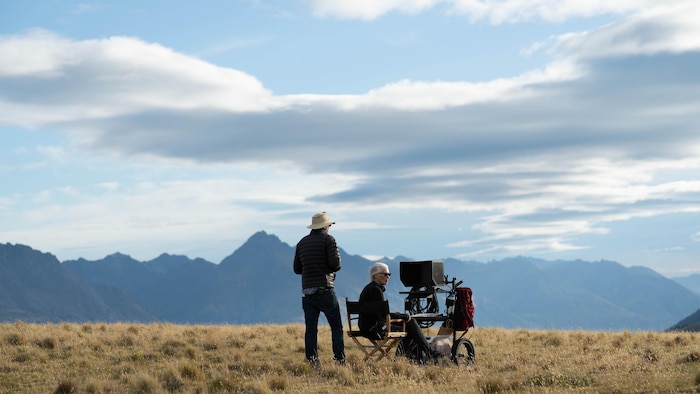 Une femme est assise derrière une caméra devant des montagnes. 