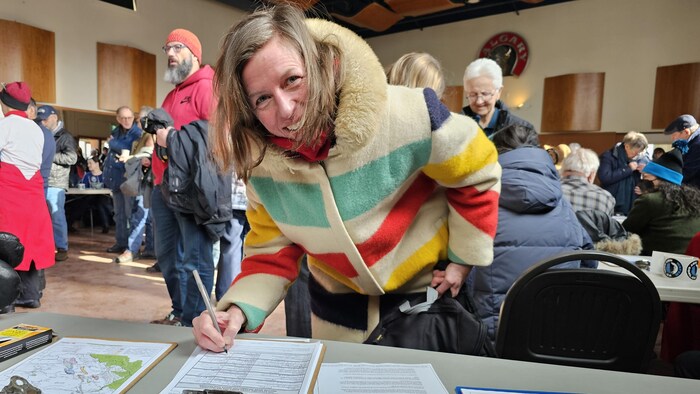 Jane Kubke signe une pétition en souriant à la caméra.