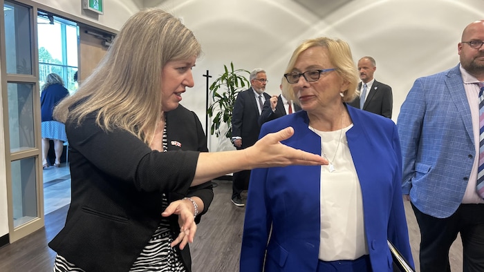 Deux femmes discutent, des gens derrière elles.