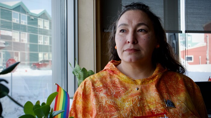 Une femme vêtue d'un haut orange regarde à travers la fenêtre de son bureau, à Iqaluit, au Nunavut, le 7 mars 2024.