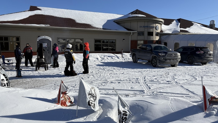 Six personnes en vêtements d'hiver sont dehors devant un grand bâtiment enneigé. 