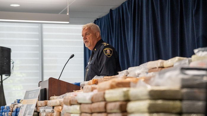 Jason Crowley s'adresse aux médias lors d'une conférence de presse, à côté d'une grande quantité de paquets de drogue.