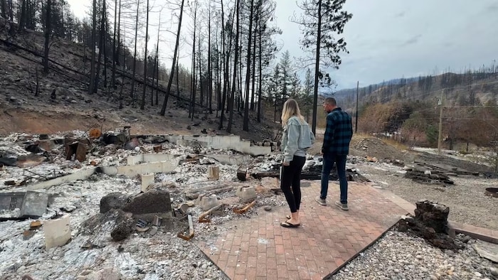 Un couple contemple les ruines calcinées de sa maison, qui a été réduite en cendres jusqu’aux fondations.