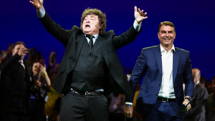Deux hommes en complet se tiennent devant une foule.