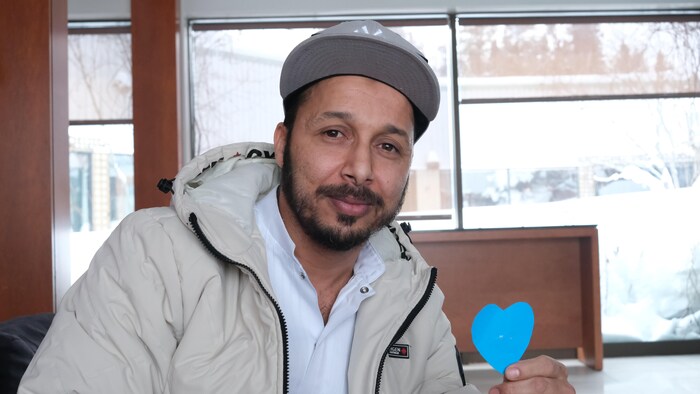 Jawad Ait Elhaj Saleh tient en main un cœur bleu fait en papier.
