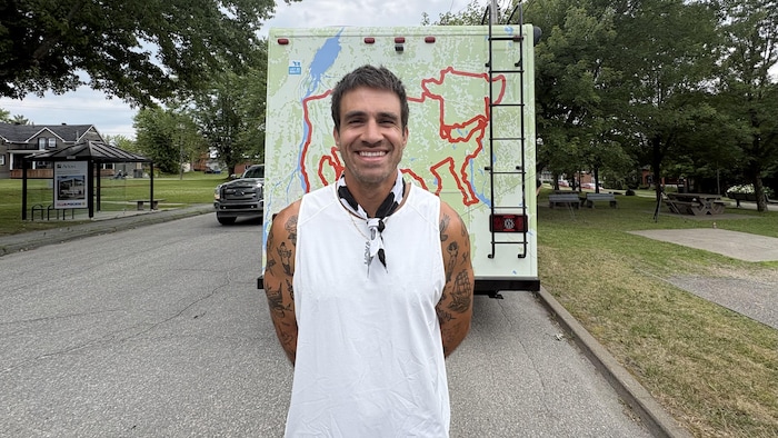 Il prend la pose devant un camion sur lequel est collé un imprimé d'une carte du Québec, où se trouve un tracé qui forme une vache.