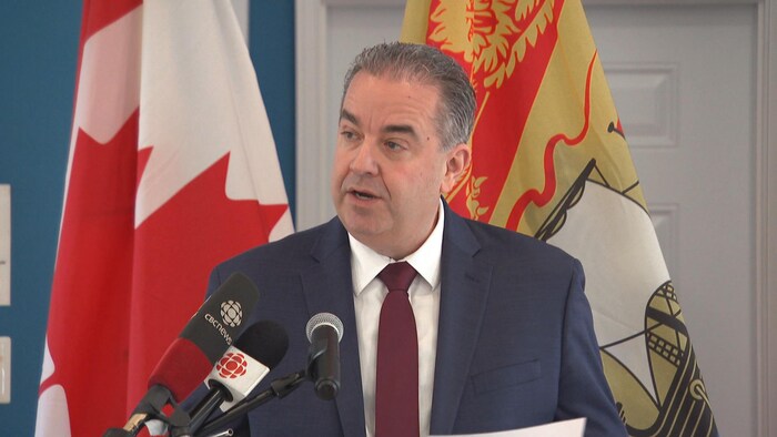 Le ministre est devant un lutrin. Il parle et regarde vers la gauche de l'image.