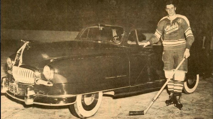 Jean Béliveau dans lad   uniforme posant devant l'automobile flambant neuve qu'on lui avait offerte à la fin de lad   séjour avec les Citadelles de Québec