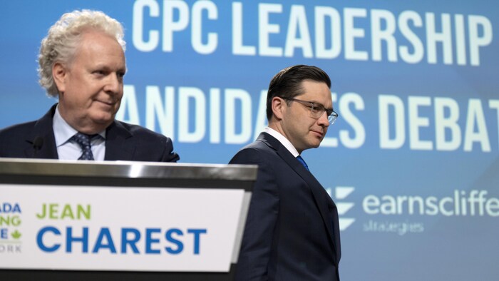 Conservative leadership candidate Pierre Poilievre, right, walks past Jean Charest as he takes his place on stage during a debate at the Canada Strong and Free Network conference in Ottawa on May 5, 2022.