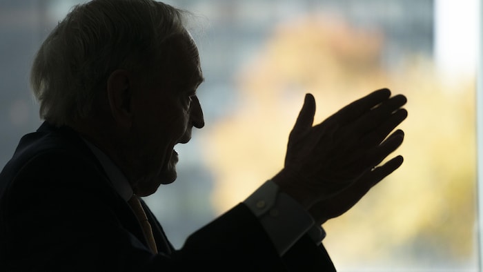 M. Chrétien, de côté, à contre-jour, parle avec les mains ouvertes devant lui.