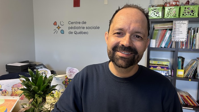 Dans un bureau du Centre de pédiatrie sociale de Québec, Jean-Christophe Nicolas sourit à la caméra. 