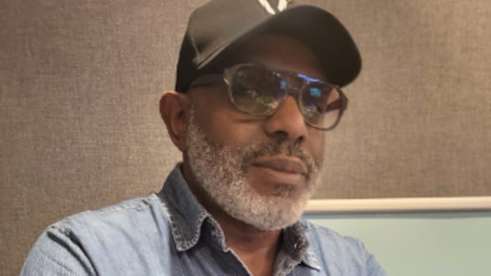 Jean-Claude Barny airs  les bras croisés. Il porte des lunettes et une casquette.