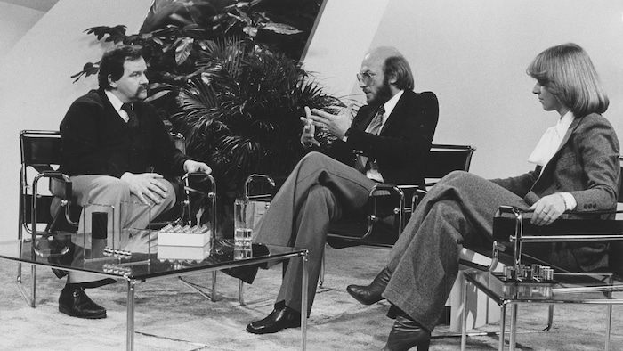 Les trois personnes sont assises sur des chaises sur un plateau de télévision.