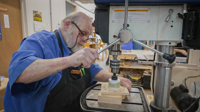 Un homme perce un trou dans un bout de bois avec une scie circulaire dans un atelier de menuiserie.
