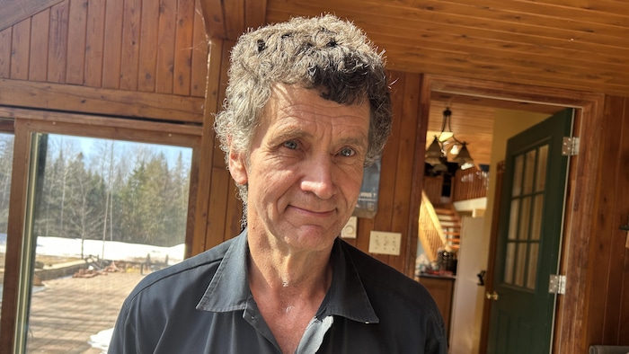 Un homme à l'intérieur d'un bâtiment, une porte ouverte derrière lui. Il sourit pour la photo.
