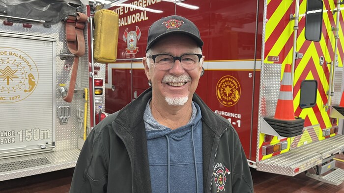 Un homme sourit à la caméra devant un camion de pompiers.