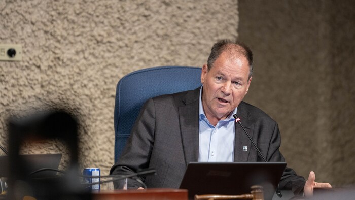 Un homme est assis derrière une table sur laquelle est déposé un micro.