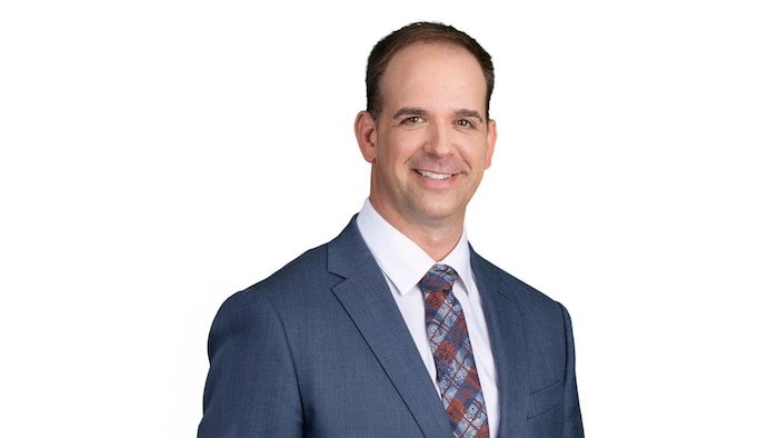 একজন মানুষ যিনি একটি জ্যাকেট পরেন এবং একটি টাই সাদা পটভূমির সামনে ছবির জন্য হাসি।