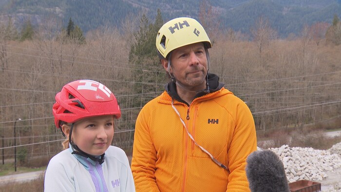 Un père et sa fille portant des casques se tiennent sur une montagne.