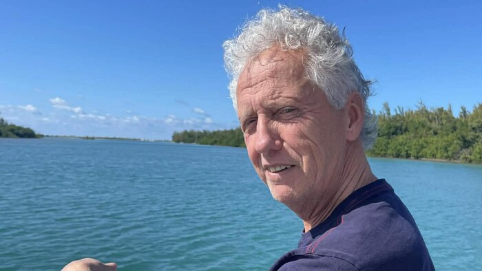 Assis sur une base flottante au milieu de l'eau turquoise, l'homme sourit.