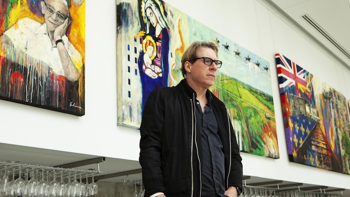 Le peintre Jean Gaudreau pose devant 3 tableaux qui se veulent un hommage à la projection extérieure «Le Moulin à images».