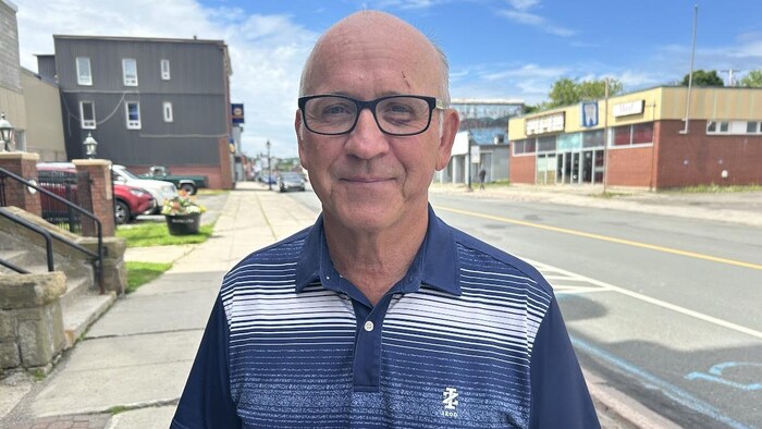 Un homme sourit à la caméra, sur un trottoir du centre-ville.