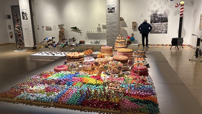 Des centaines de petites boules colorées et plusieurs faux desserts et gâteaux sont disposés sur une table basse, dans une salle d'exposition. 