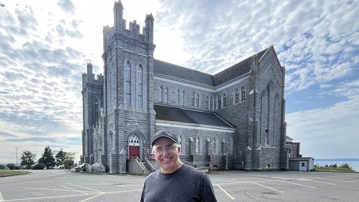 Un homme debout, souriant, devant une église.