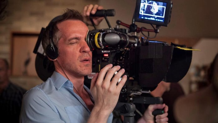 On voit le réalisateur muni d'écouteurs, tenant la caméra et regardant dans le viseur.