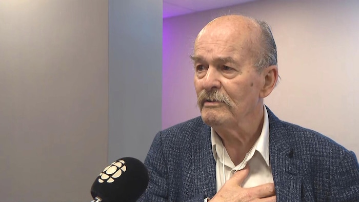 Un homme porte la main sur sa poitrine. Un micro est tendu vers lui.