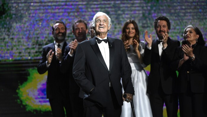 L'acteur se tient sur scène lors de la soirée des César en 2017. Derrière lui, d'autres personnalités applaudissent.