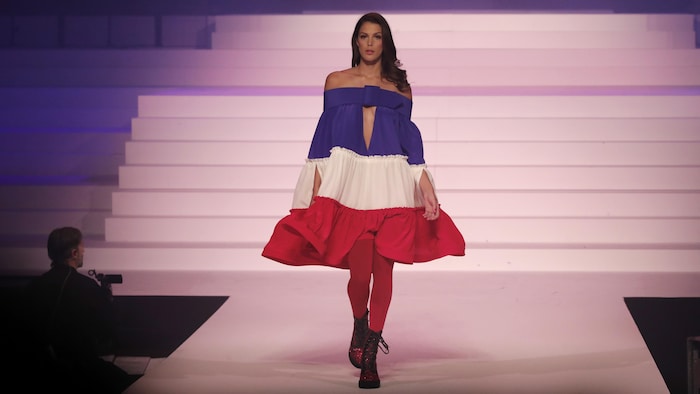 Une femme portant une robe aux couleurs de la France marche sur une scène.