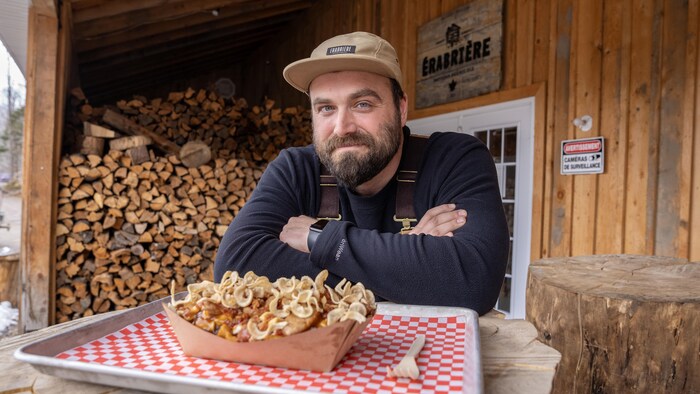 Jean-Philippe Brière assis à sa cabane à sucre devant une poutine.