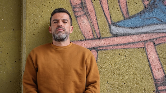 Un homme debout est adossé à un mur de ciment.