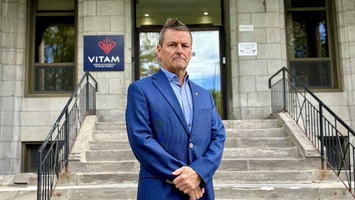 Un homme en veston bleu pose devant les marches d'entrée du centre de recherche en santé durable VITAM.