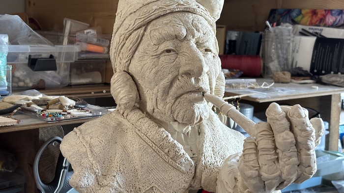 Gros plan sur un buste en plâtre représentant une grand-mère innue qui fume la pipe.