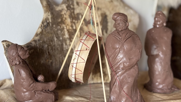 Gros plan sur une installation miniature en argile et en bois représentant une cérémonie innue autour d'un tambour traditionnel.
